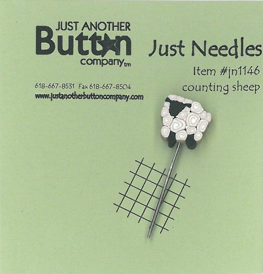 A small counting sheep pin with a white sheep head and black wool details on a silver pin, displayed on a light green card with the brand name 'Just Another Button Company' and the text 'Just Needles' and 'Item #11146 counting sheep'.
Photo by JustAnotherButtonCompany.com [image_link]