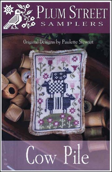 A cross stitch embroidery kit depicting three cows standing on a hillside with flowers, placed on a pincushion.
Photo by PlumStreetSamplers.com [image_link]