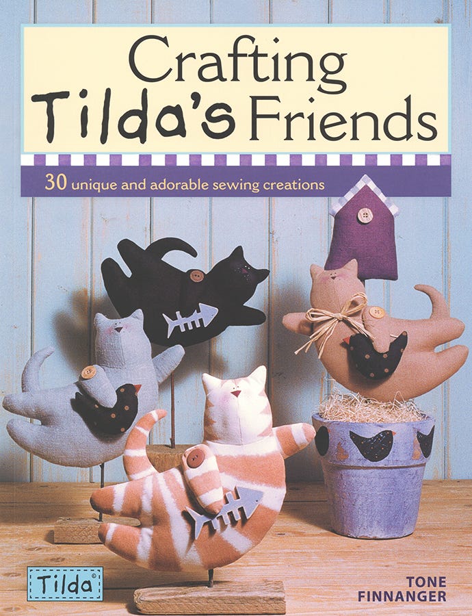 Front cover of the book 'Crafting Tilda's Friends' by Tone Finnanger, showing several handmade cat and bird sewing creations displayed on a wooden surface against a light blue paneled background.
Photo by Tildafabrics.com [image_link]