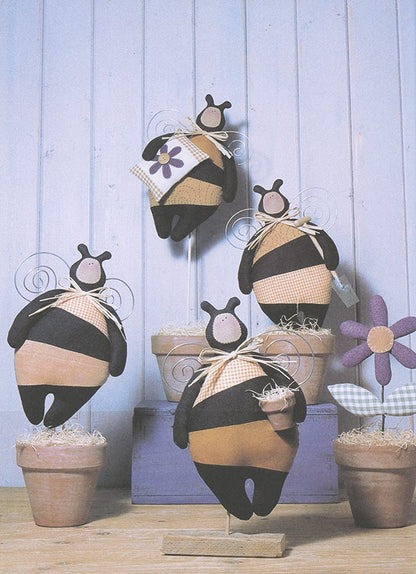 A set of handmade bumblebee wall decorations in terracotta pots, featuring black and tan striped fabric bunnies with purple flower accents, arranged against a light blue wooden paneled background.
Photo by Tildafabrics.com [additional_image_link]