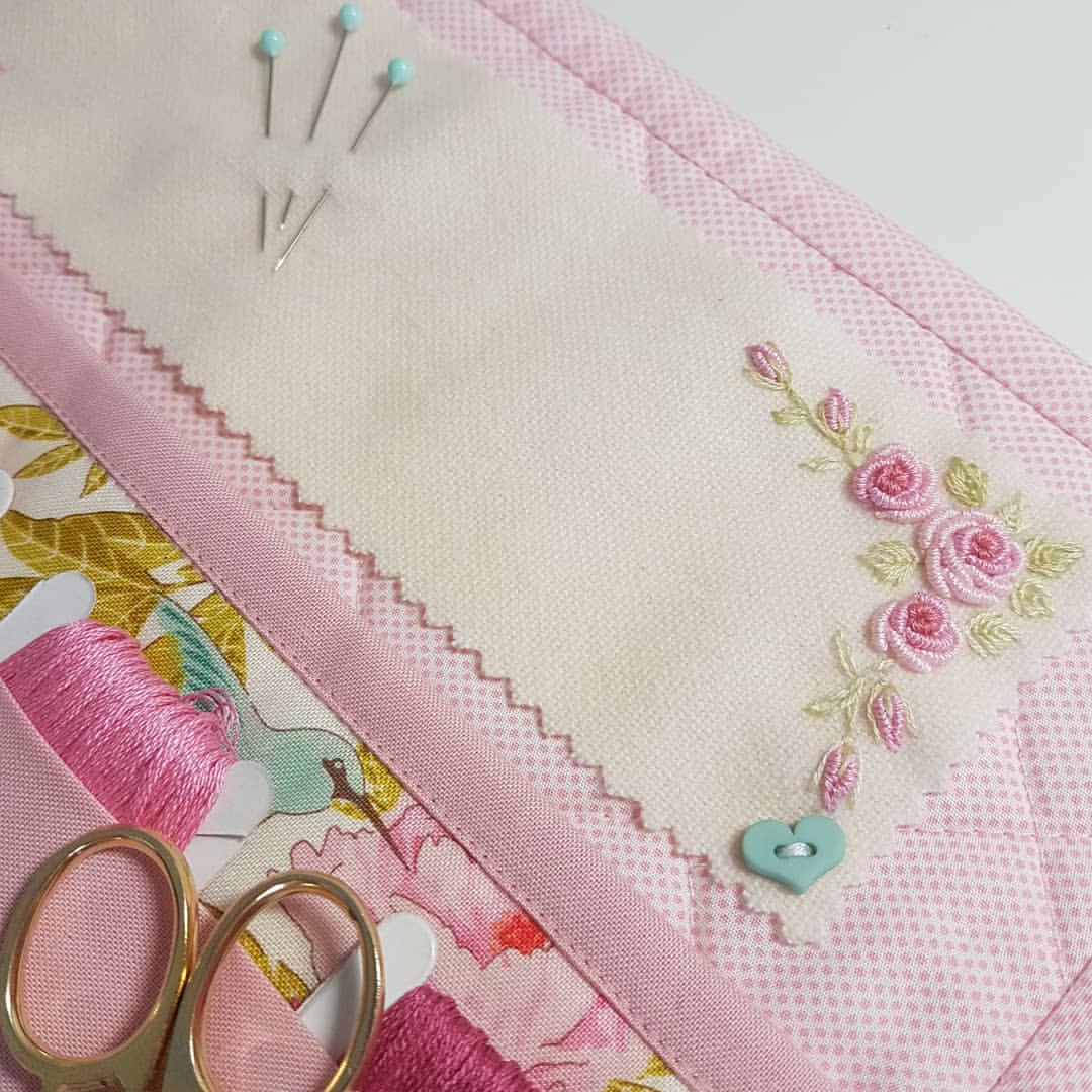 A close-up of a pink quilted fabric organizer or pouch with floral embroidery, pins, scissors, and thread on a white background.
Photo by Angela Watson [additional_image_link]