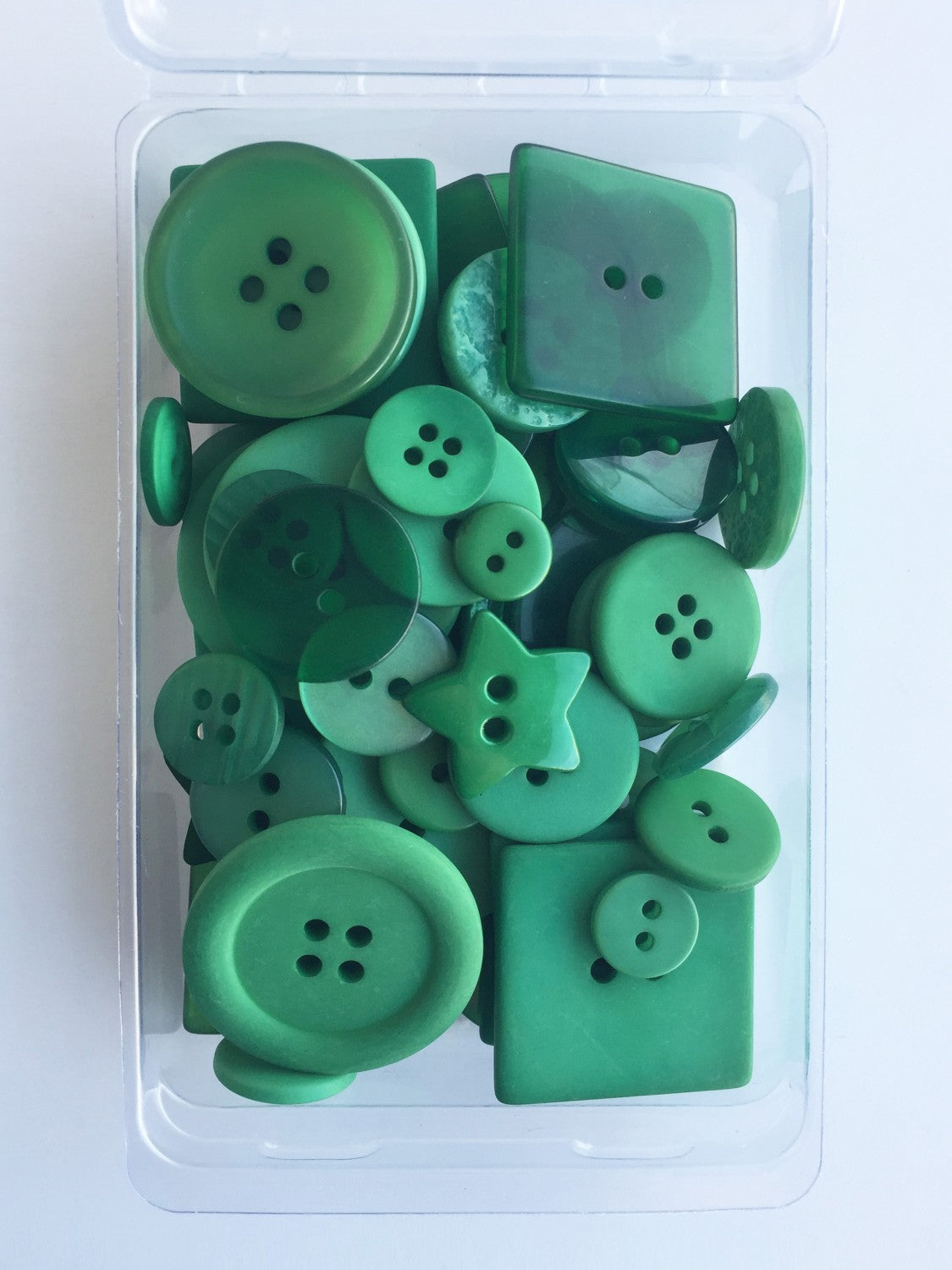 A collection of 55 green buttons in various sizes placed in a clear plastic case, with visible shiny surfaces and varied shapes including round, star, and other designs typical for crafting purposes.
Photo by JustAnotherButtonCompany.com [image_link]