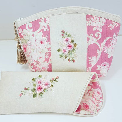 A matching fabric pouch and clutch set in a pink and cream floral patchwork design, featuring embroidered pink rose motifs and a gold tassel zipper pull.
Photo by Angela Watson [image_link]
