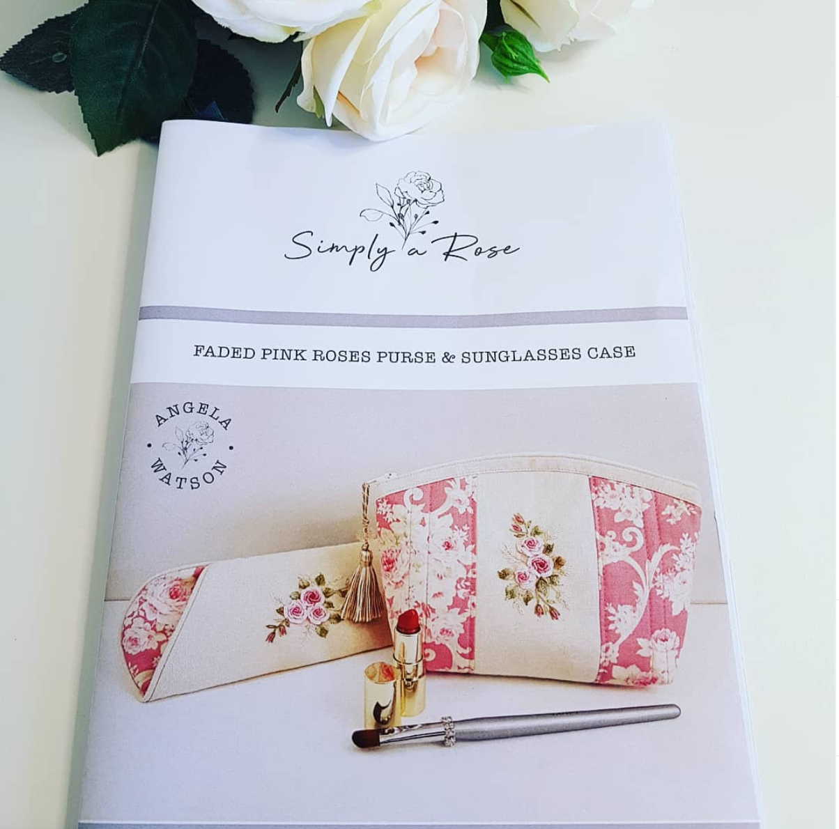 A fabric cosmetic pouch set with a matching sunglasses case by Simply a Rose, featuring a cream and faded pink rose floral pattern. The products are displayed on a light cream background with white roses and green leaves as props.
Photo by Angela Watson [additional_image_link]