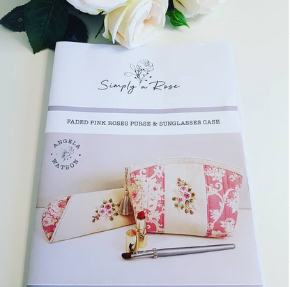 A fabric cosmetic pouch set with a matching sunglasses case by Simply a Rose, featuring a cream and faded pink rose floral pattern. The products are displayed on a light cream background with white roses and green leaves as props.
Photo by Angela Watson [additional_image_link]