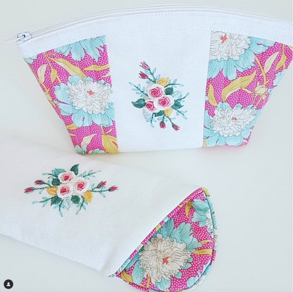 A white zippered pouch with floral fabric panels on the sides and center, shown closed from the front and folded to reveal the patterned interior. The pouch has a white zipper, white fabric body, and pink, blue, green, and yellow floral print.
Photo by Angela Watson [additional_image_link]