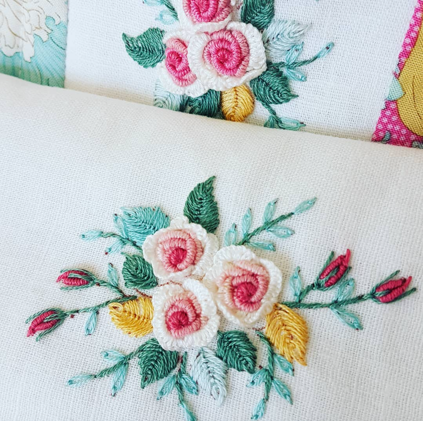 Close-up of embroidered floral fabric with pink and white roses, green leaves, and yellow accents on a cream textile background.
Photo by Angela Watson [additional_image_link]