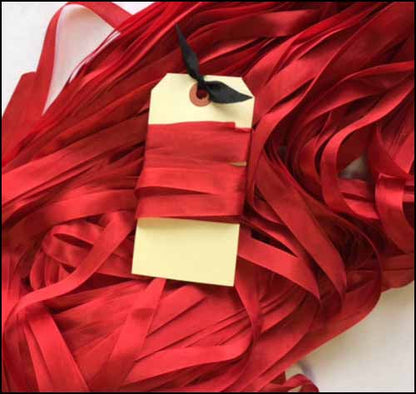 A close-up of a loose bundle of shiny red satin ribbon with a blank cream gift tag wrapped around it and a small black ribbon bow at the top, set against a white background.
Photo by LadyDotCreates.com [additional_image_link]