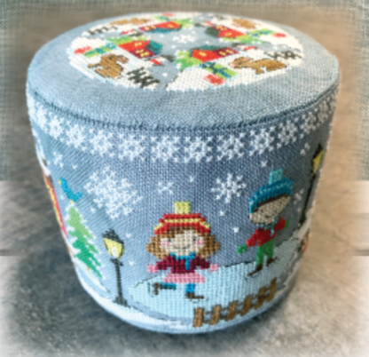 A round, low-profile pouf ottoman featuring a light blue winter-themed cross-stitch pattern with children ice skating, snowflakes, and a festive top design.
Photo by Tiny Modernist [image_link]