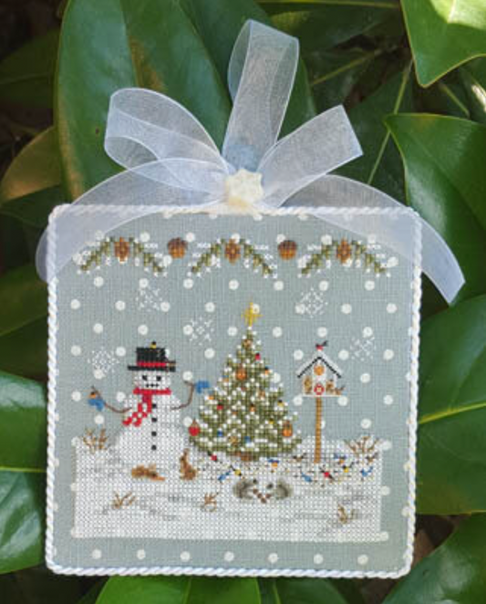 A cross stitch kit pattern depicting a Christmas ornament with a snowman, a Christmas tree, and decorative elements on a blue linen background with white polka dots.
Photo by Blackberry Lane Designs [image_link]