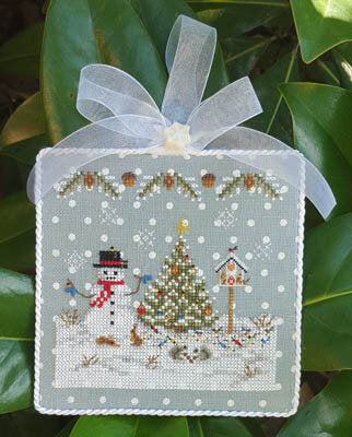 A cross stitch kit pattern depicting a Christmas ornament with a snowman, a Christmas tree, and decorative elements on a blue linen background with white polka dots.
Photo by Blackberry Lane Designs [additional_image_link]