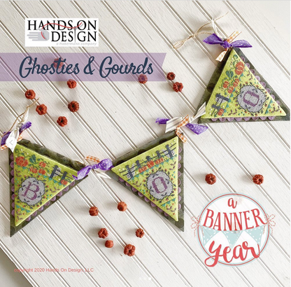 Three triangular fabric bunting flags with floral embroidery and purple ribbon bows, arranged on a white wood plank surface with scattered dried red berries. Text overlays read 'HANDS ON DESIGN', 'Ghosties & Gourds', and 'a BANNER year'.
[image_link]