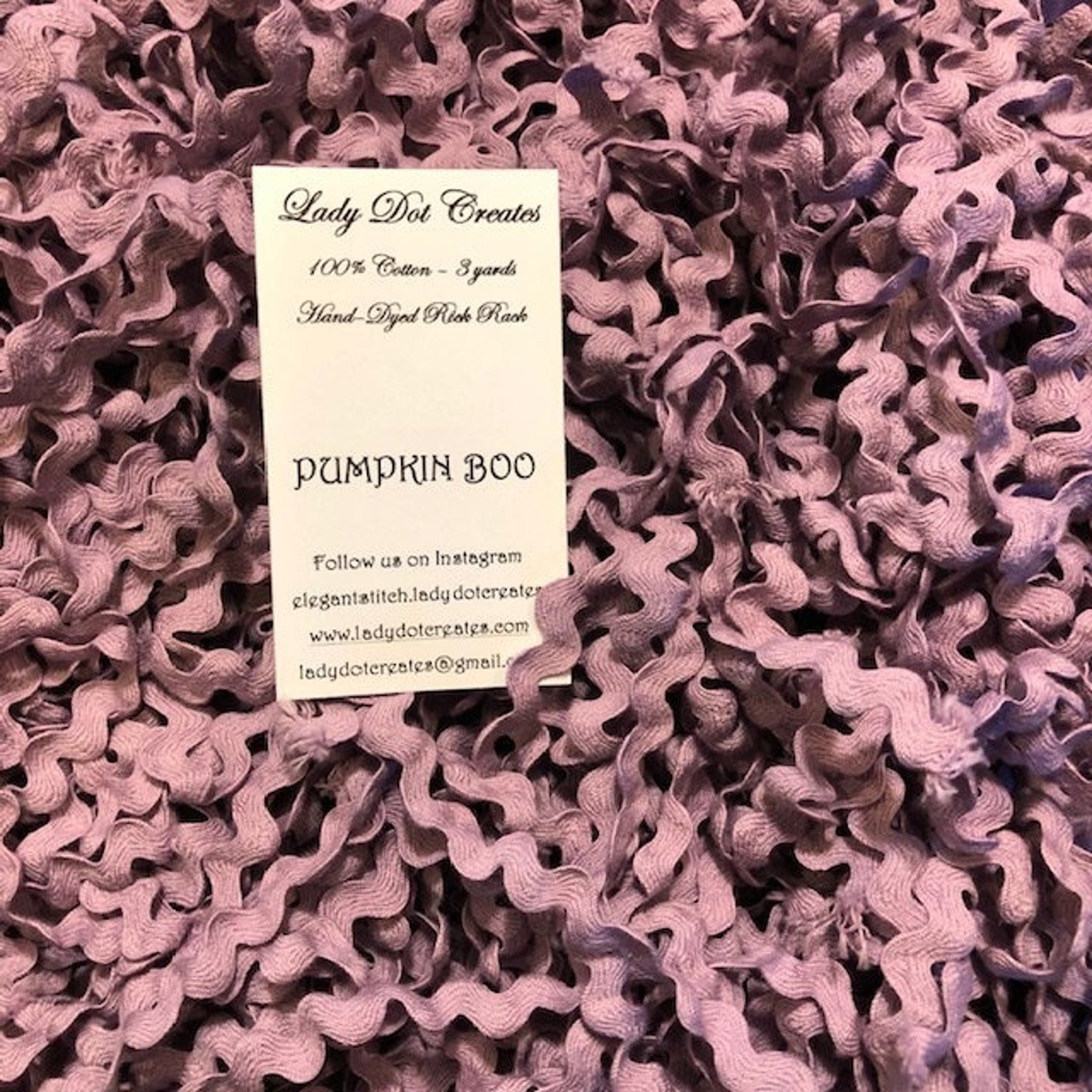 A close-up of ric rac yardage in a dusty mauve-purple color, with a white paper label card reading 'Lady Dot Creates' and 'Pumpkin Boo' placed on top.
[additional_image_link]
