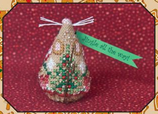Cross stitch embroidery kit depicting a gingerbread jingle mouse with a green ribbon, gold swirl hanger, and red and green floral details, on a red background.
Photo by JustNan.com [additional_image_link]