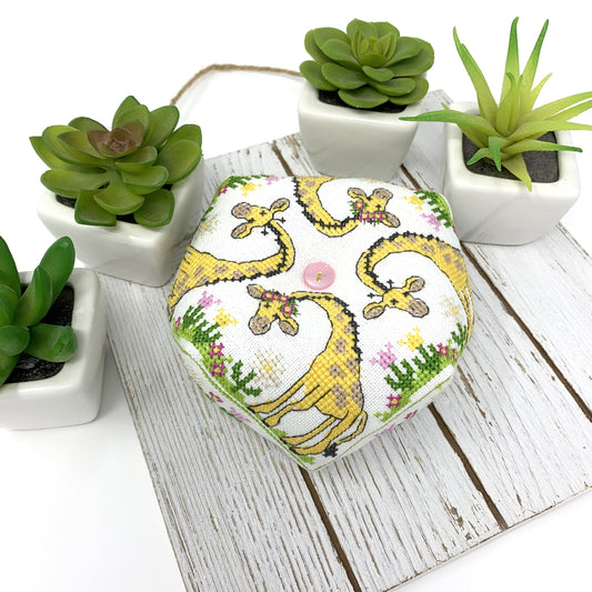 A hexagonal fabric-covered item, likely a small box or cushion, featuring a playful giraffe print on a white background. It is styled on a white wooden board surrounded by small potted green succulents.
Photo by Tiny Modernist [image_link]