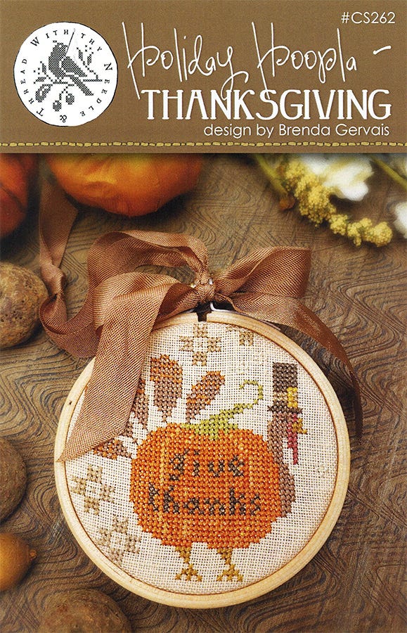 A cross stitch embroidery kit depicting a Thanksgiving theme, with a design featuring an orange pumpkin, a turkey, and text elements on a beige background, complete with a brown ribbon and tan seam binding.
Photo by With Thy Needle & Thread [image_link]