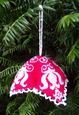 A red cross stitch bell shaped ornament kit with white embroidery and beads, hanging from a tree.
 [image_link]