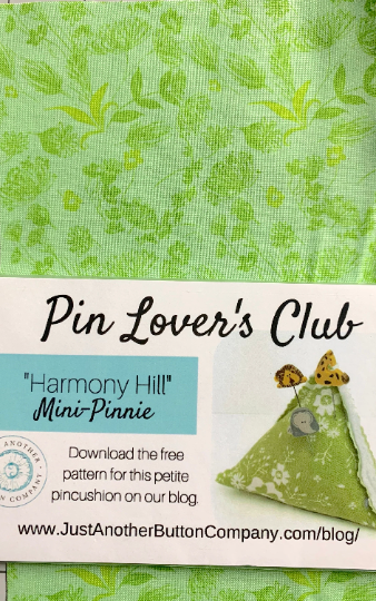 A green patterned fabric swatch with a white banner reading 'Pin Lover's Club' and 'Harmony Hill Mini-Pinnie,' plus a small photo of a finished green pincushion and the website JustAnotherButtonCompany.com.
Photo by TheSurgeonsKnots.com [additional_image_link]