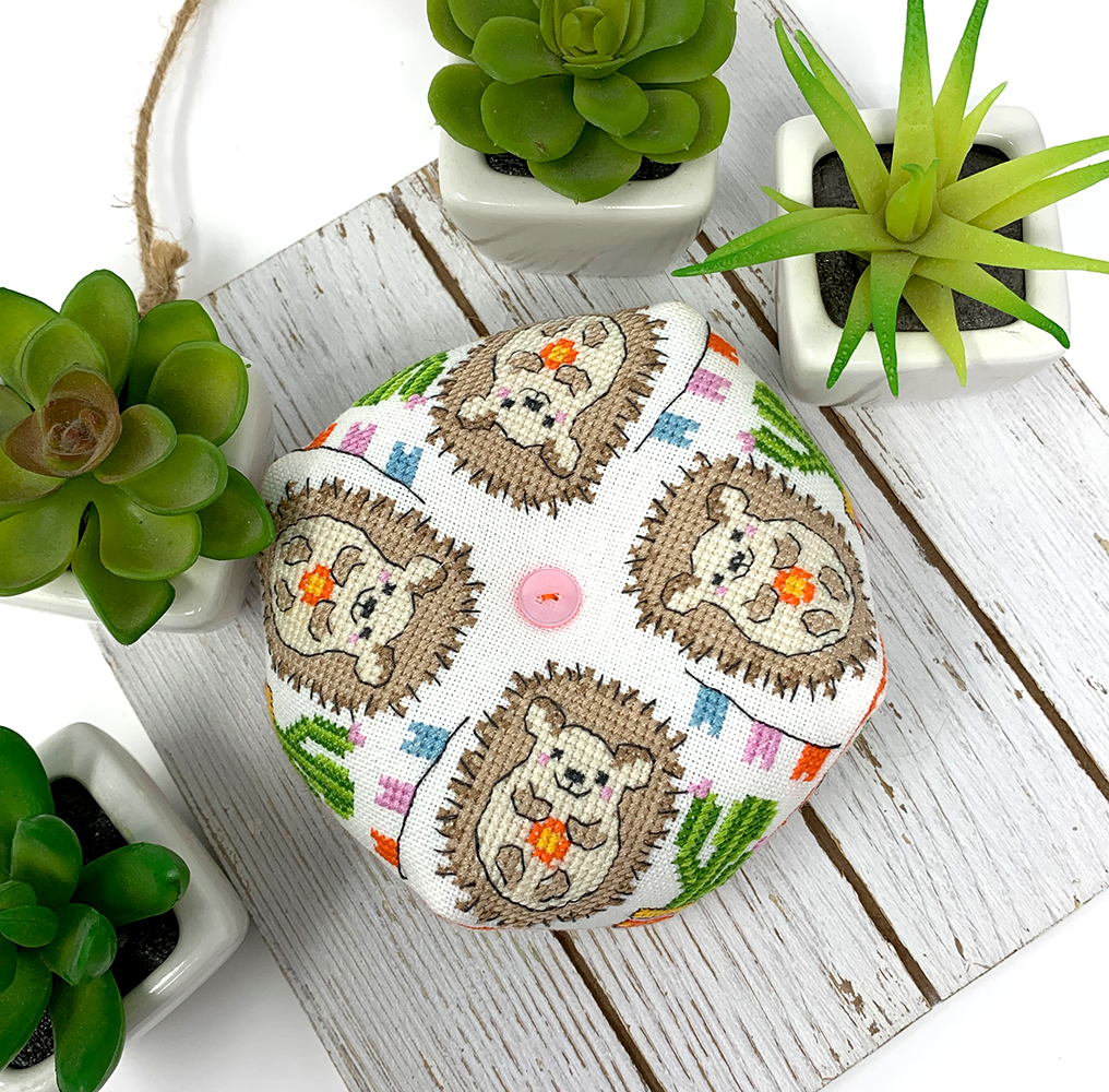 A small round fabric cushion or pillow with a repeating hedgehog pattern, styled on a white wooden board with potted succulents around it.
Photo by Tiny Modernist [additional_image_link]