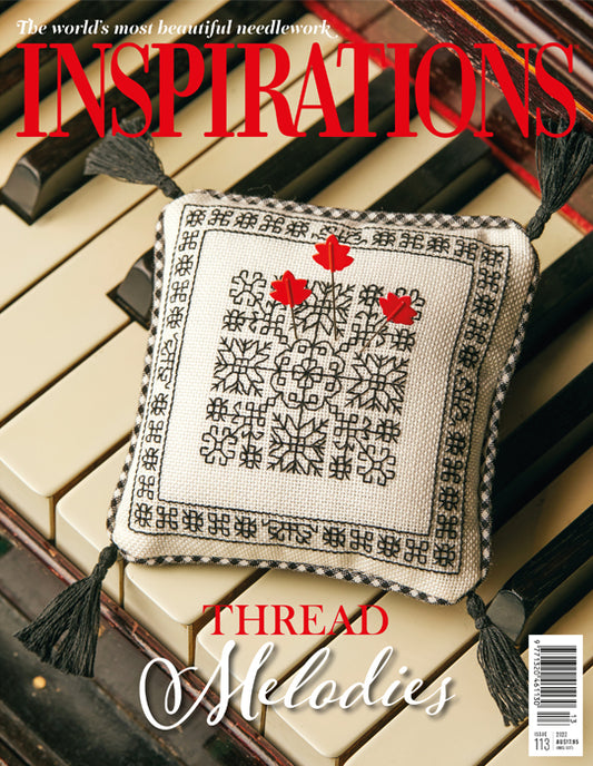Cover of a needlework magazine or book titled "INSPIRATIONS" with a decorative embroidered pillow placed on piano keys. The pillow is cream with black embroidered snowflake and border patterns and red embroidered hearts.
Photo by InspirationsStudios.com [image_link]