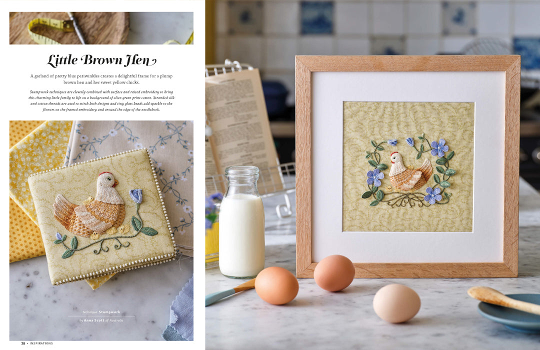 A framed handmade quilt featuring a brown hen and blue flowers on a beige background, displayed in a light wood frame on a kitchen counter next to eggs, a glass bottle of milk, and a cookbook. The left page of a book shows the title 'Little Brown Hen'.
Photo by InspirationsStudios.com [additional_image_link]