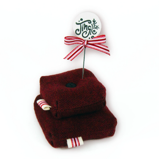 A red herringbone wool pincushion kit with a 'Jingle' brand pin attached to it, designed for holiday themed crafting.
Photo by JustAnotherButtonCompany.com [image_link]
