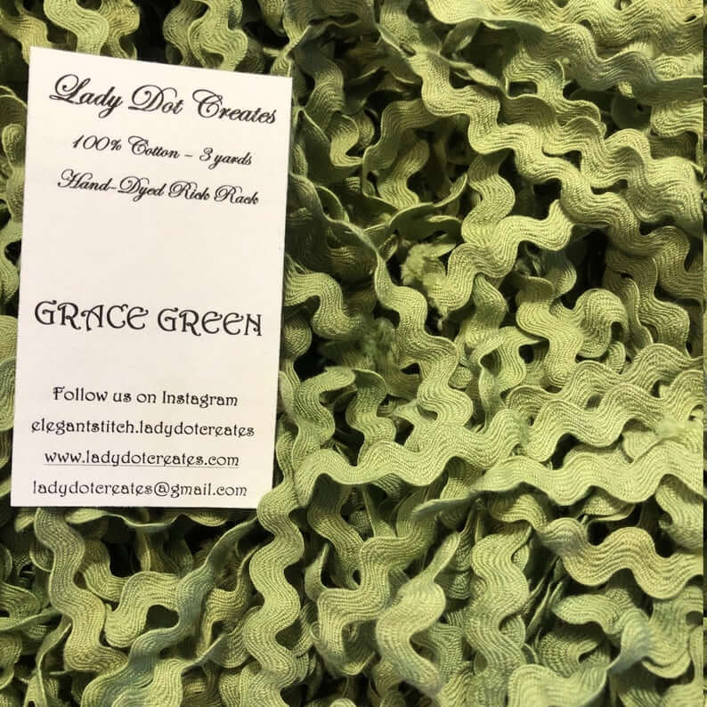 A close-up of olive green wavy ribbon trim filling the frame, with a white paper label card reading 'Lady Dot Creates' and 'GRACE GREEN' placed on top.
[additional_image_link]