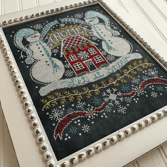 Framed cross-stitched piece with two snowmen and a house on a dark background
Photo by Handsondesign.com [image_link]