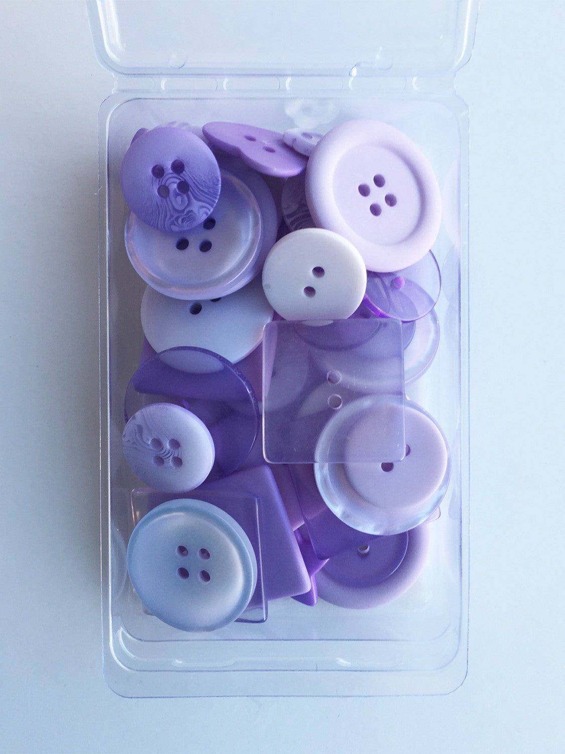 A clear plastic container holding 55 purple buttons of various sizes, ranging from 1/4 inch to 1 1/8 inch, with a solid lavender hue.
Photo by JustAnotherButtonCompany.com [image_link]