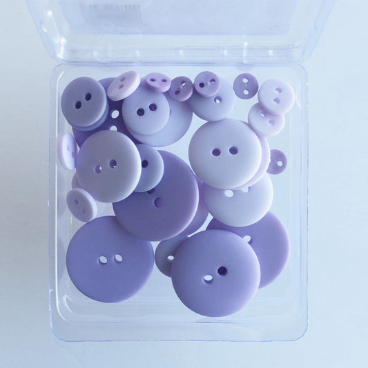A clear plastic container holding 25 purple buttons with a smooth finish, varying in sizes.
Photo by JustAnotherButtonCompany.com [image_link]