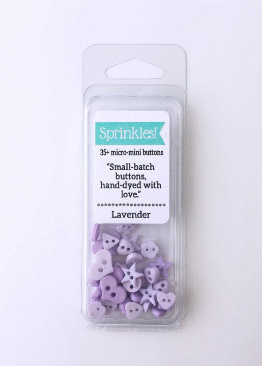 Pack of lavender-colored sprinkle buttons from Just Another Button Company, displayed in a clear plastic case, with text on the label indicating the product details and brand.
Photo by JustAnotherButtonCompany.com [image_link]