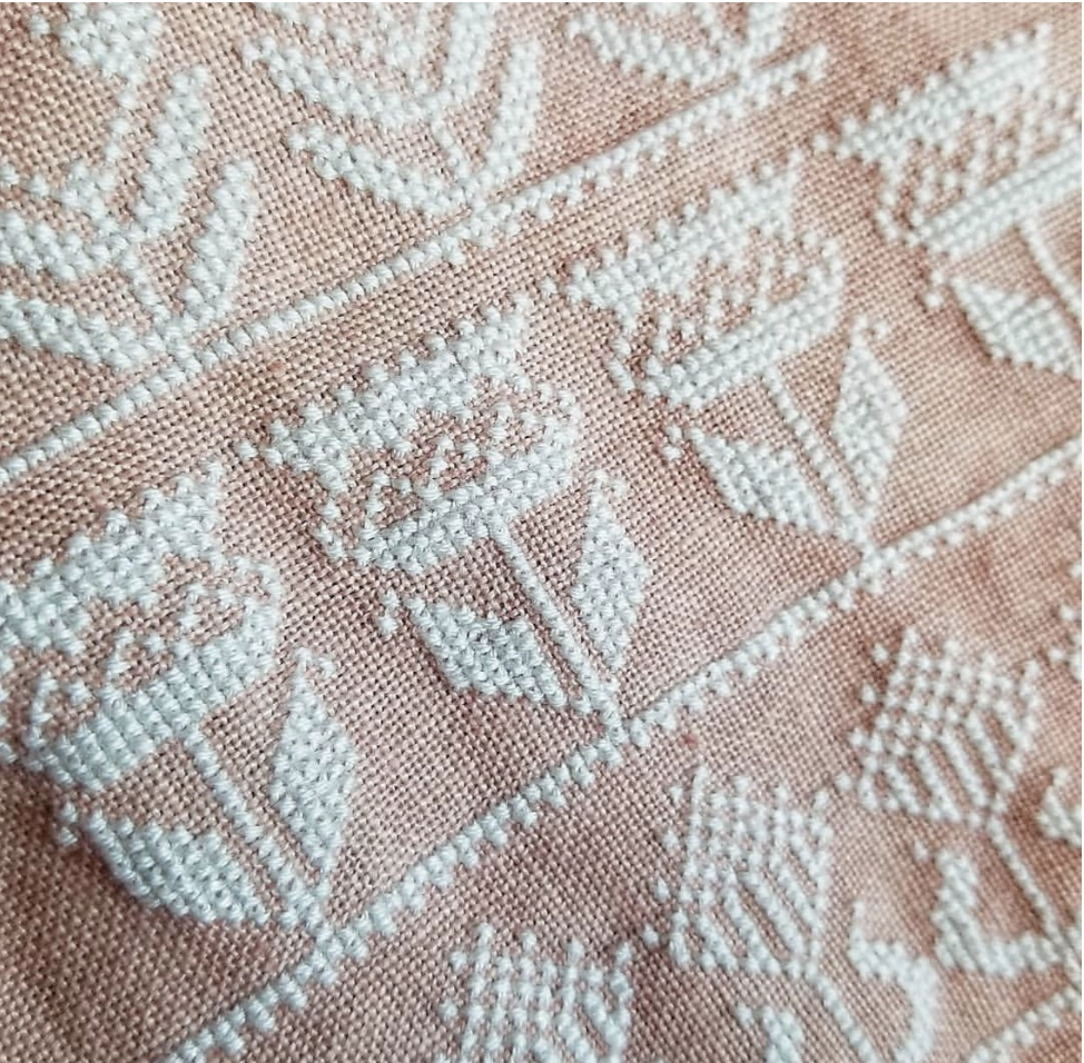 Close-up of a woven fabric with a light pink base and white embroidered floral and geometric patterns.
Photo by HelloFromLizMathews.com [additional_image_link]