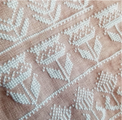 Close-up of a woven fabric with a light pink base and white embroidered floral and geometric patterns.
Photo by HelloFromLizMathews.com [additional_image_link]