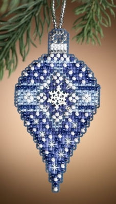 A beaded Christmas ornament shaped like a teardrop, decorated with blue, white, and silver beads in a snowflake pattern, hanging from a silver chain against a warm brown background with pine branches at the top.
Photo by Mill Hill [image_link]