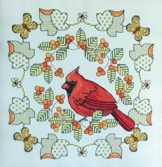 Cross stitch kit image featuring a detailed embroidery pattern of a red cardinal bird surrounded by green leaves, orange berries, and yellow butterflies on a white background.
Photo by Lesley Teare [image_link]