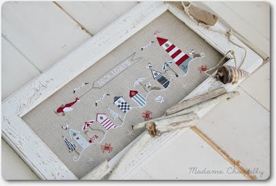 A cross stitch kit depicting a beach scene with various elements like beach houses, lighthouse, starfish, and crabs on a white background.
Photo by madamechantilly.com [additional_image_link]