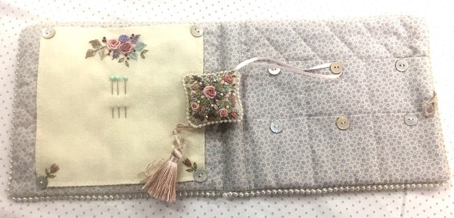 A handmade quilted fabric organizer or pouch with a floral embroidered panel on the left, a patterned gray right side, decorative buttons, and a small embroidered tassel charm.
Photo by Angela Watson [additional_image_link]