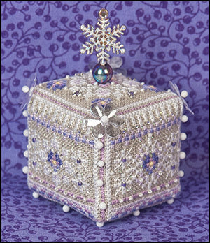 A cross-stitch embroidery kit cube ornament designed with a pansy flower with a white, silver, and purple color scheme, adorned with beads and pearls on a textured linen background.
Photo by JustNan.com [additional_image_link]