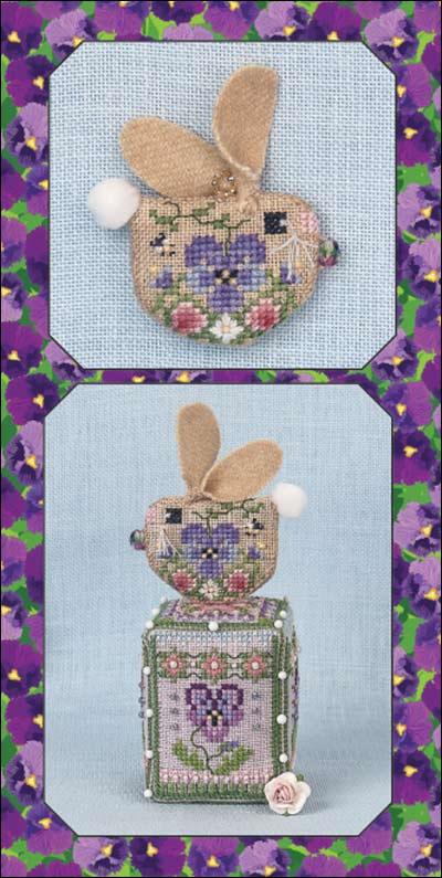A cross-stitch pattern or kit shown in two views: a small embroidered bunny head with tan ears and a floral face on a light blue square, and a larger bunny-themed cube box with a matching embroidered face. The background is a purple floral border.
Photo by JustNan.com [additional_image_link]