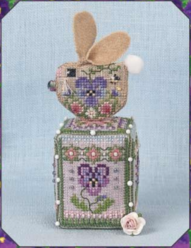 A decorative embroidered bunny-shaped figure with a floral design, featuring a small bunny head with tan ears on top of a square cube, set against a light blue textured background.
Photo by JustNan.com [additional_image_link]