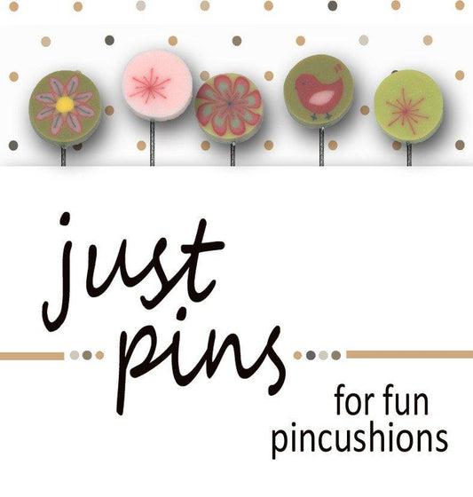A product display for 'just pins for fun pincushions' featuring five decorative circular pins on metal stands against a white background with gold polka dots. The pins include floral, geometric, and bird designs in muted green, pink, and yellow tones.
Photo by JustAnotherButtonCompany.com [image_link]