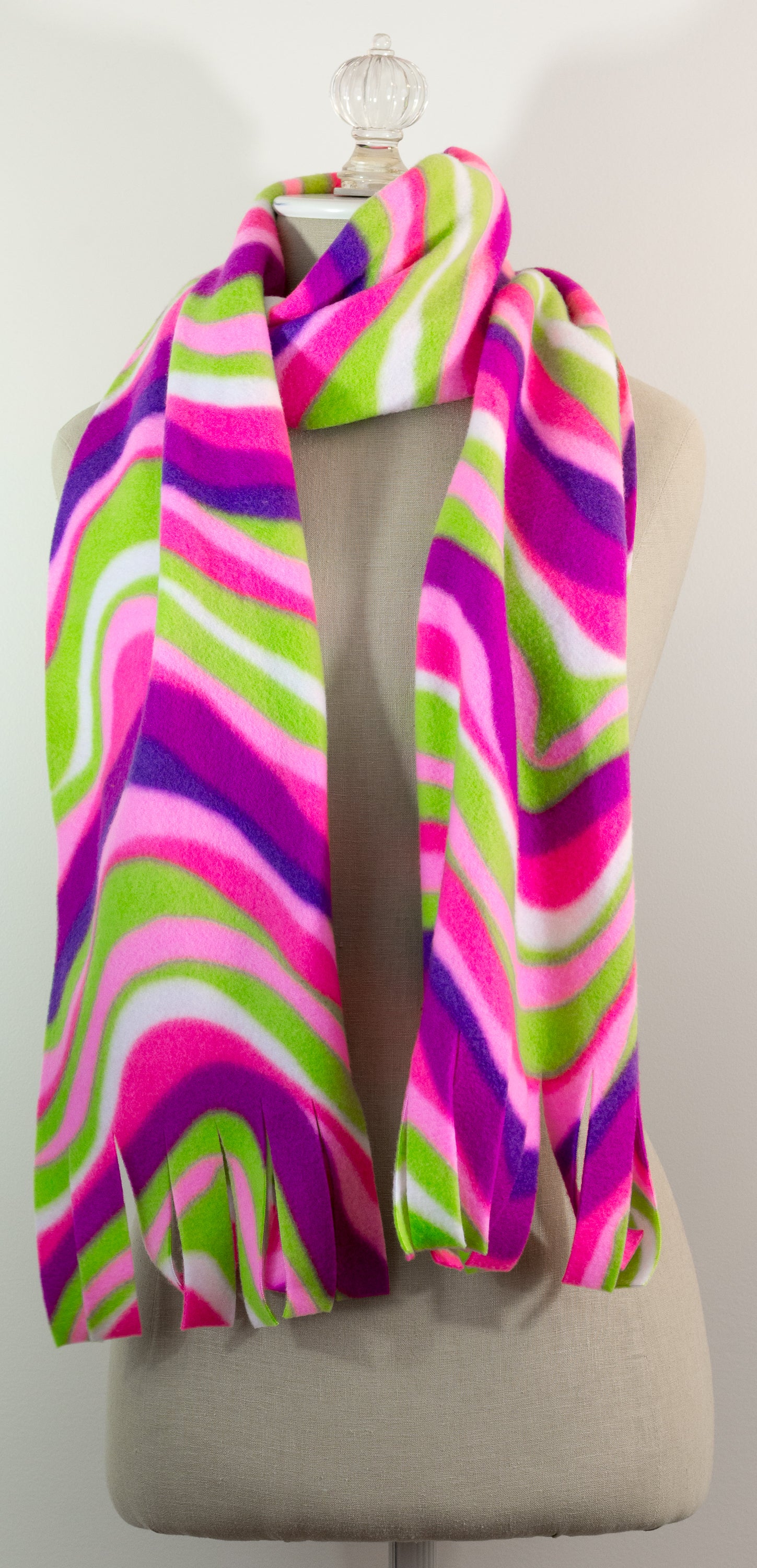 A scarf with a striped pattern featuring pink, green, white, and purple colors, displayed on a mannequin.
Photo by The Surgeon's Knots [additional_image_link]