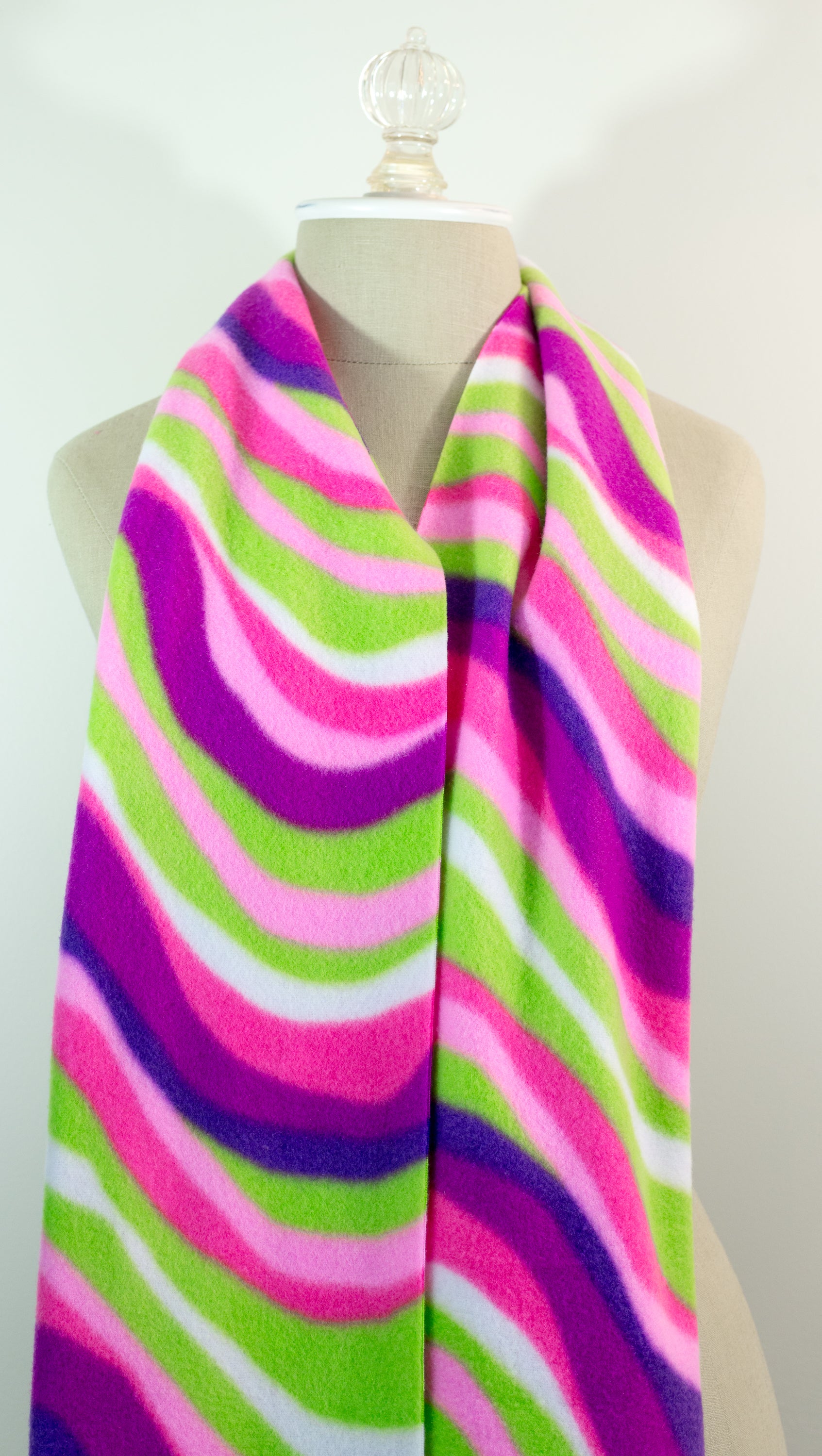 A scarf with a striped pattern featuring pink, green, white, and purple colors, displayed on a mannequin.
Photo by The Surgeon's Knots [additional_image_link]