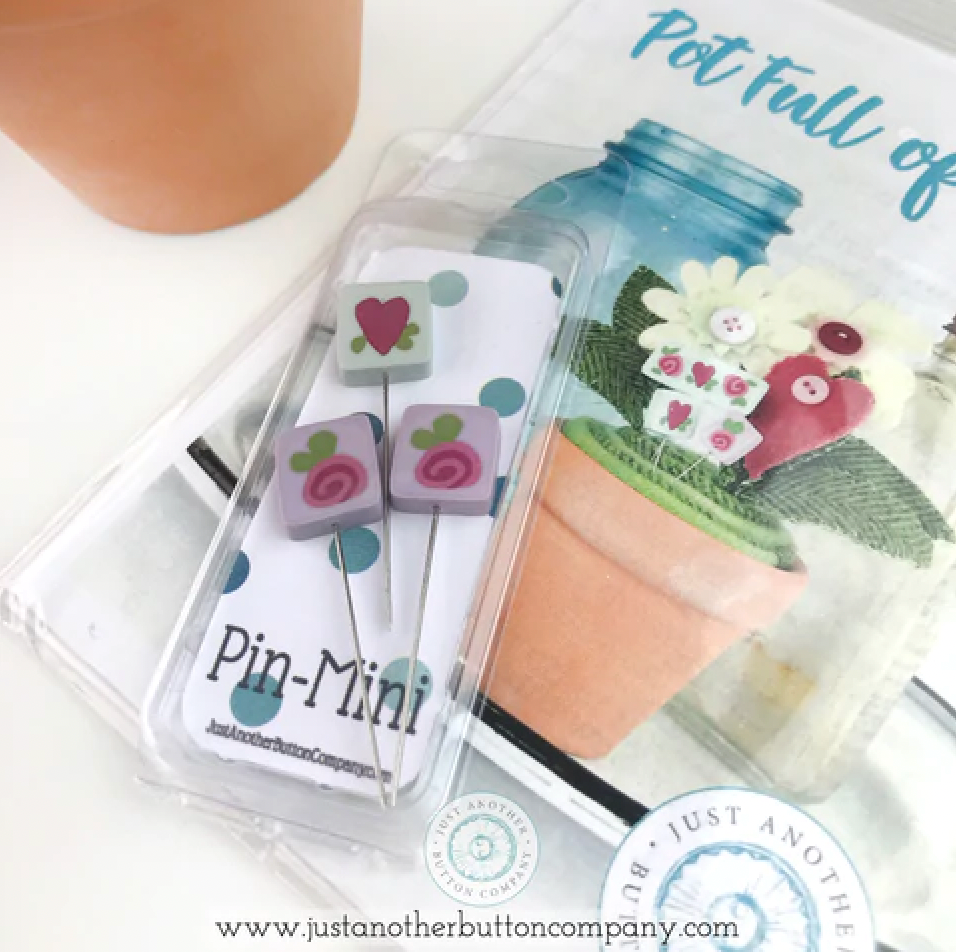 A set of small decorative buttons with metal pins, packaged in a clear plastic case on a white card. The buttons feature pink and purple floral designs with green and blue accents.
Photo by JustAnotherButtonCompany.com [additional_image_link]