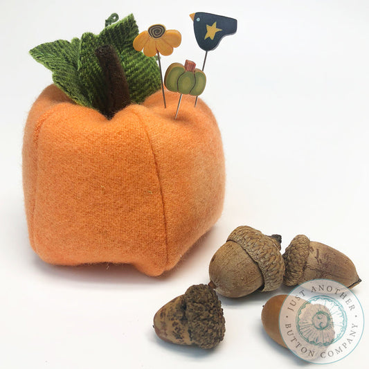 An orange felt pumpkin-shaped decorative holder with green fabric leaves and wooden pick accents, shown on a white background with acorns and a watermark for Just Another Button Company.
Photo by JustAnotherButtonCompany.com [image_link]