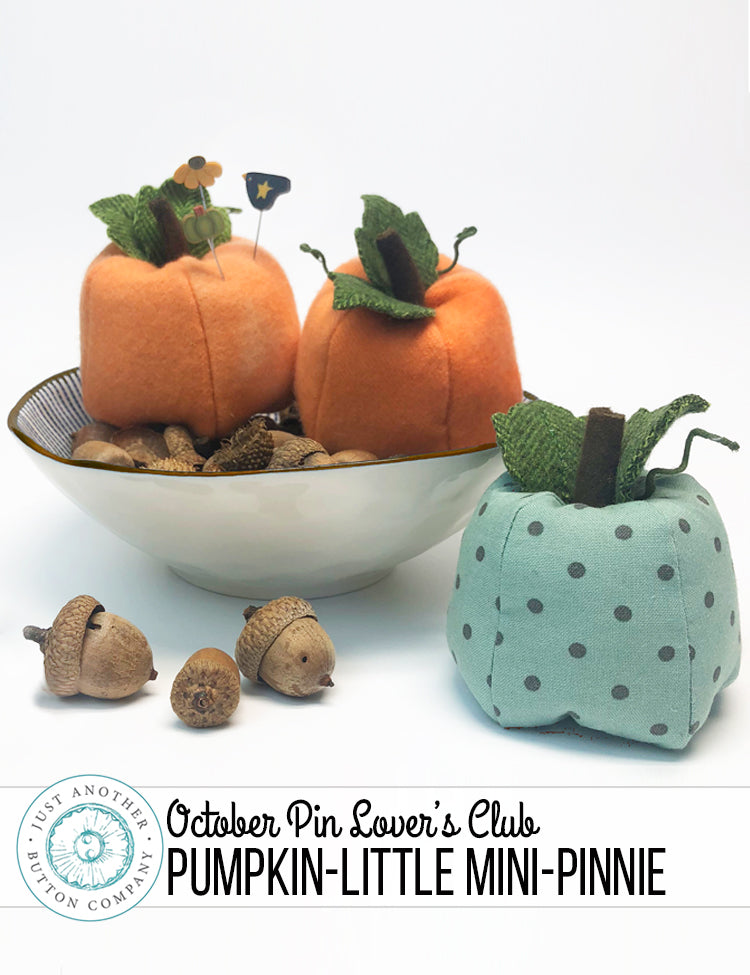 Two mini pumpkin-shaped fabric pins displayed on a white background, one orange with a small acorn and leaf decoration on top, and one light blue with dark blue polka dots. A white bowl with acorns sits behind them, and a banner at the bottom reads 'October Pin Lover's Club PUMPKIN-LITTLE MINI-PINNIE'.
Photo by JustAnotherButtonCompany.com [additional_image_link]