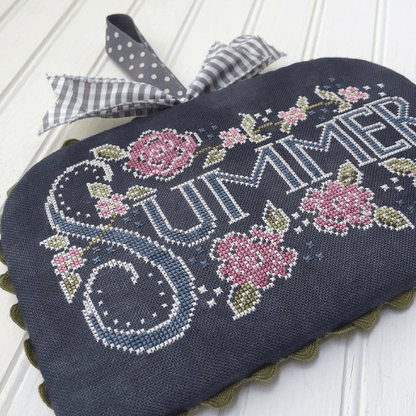 A dark charcoal woven linen summer-themed decorative piece with embroidered floral motifs and the word 'SUMMER' in large stitched letters, finished with a gray-and-white gingham ribbon bow, shown on a white paneled surface.
Photo by HandsOnDesign.biz [additional_image_link]
