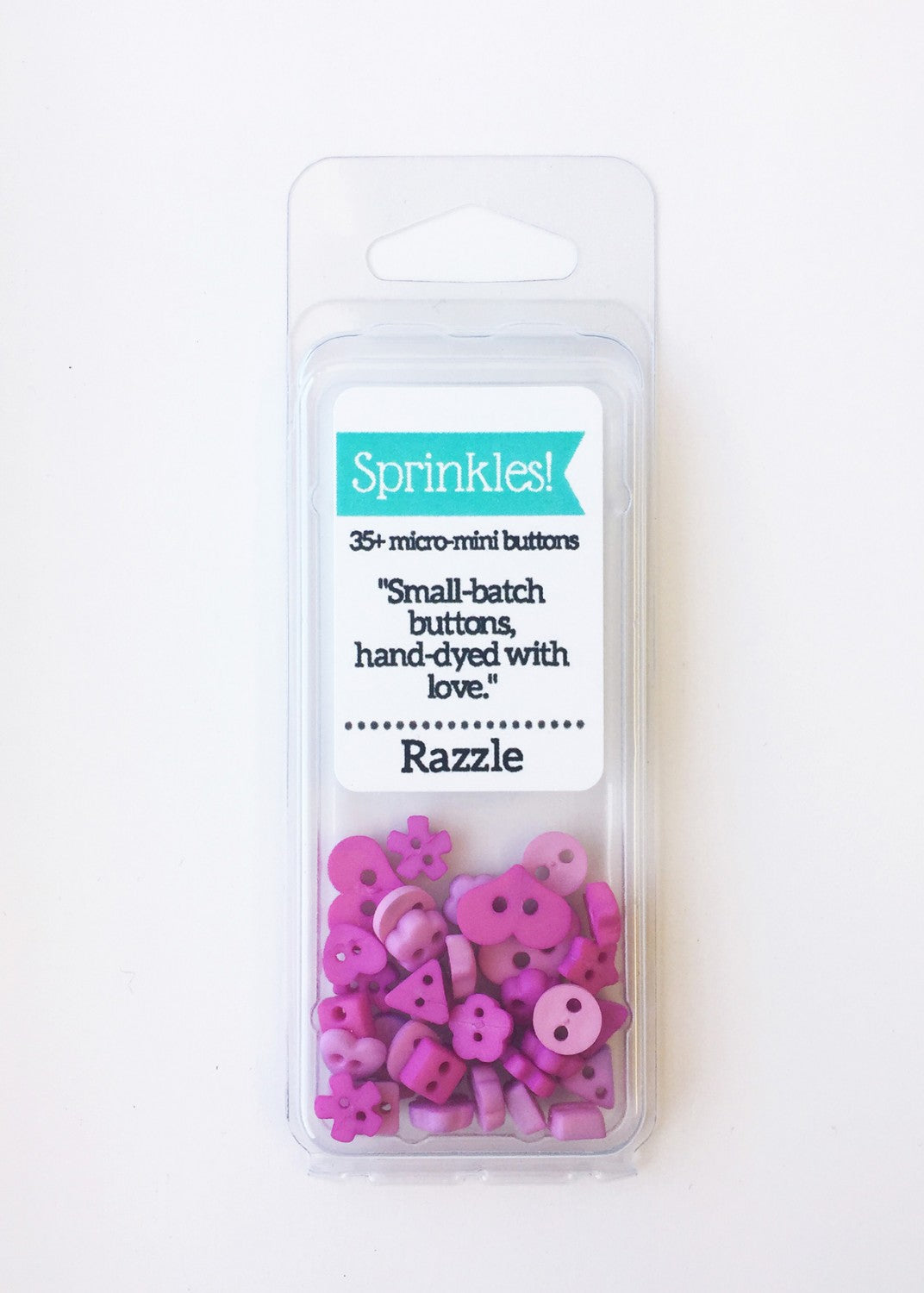 Packaging of Just Another Button Company's Razzle Sprinkle Button Pack, displaying various hand-dyed purple and pink buttons through a clear plastic window.
Photo by JustAnotherButtonCompany.com [image_link]