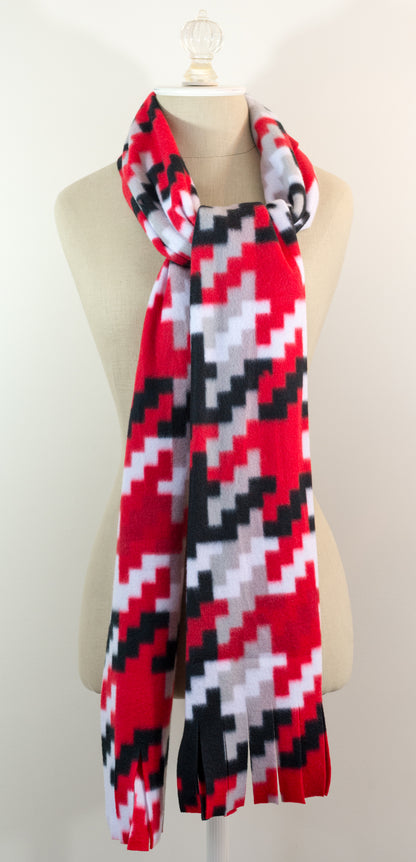 A scarf with a geometric houndstooth pattern in red, black, white, and beige colors, displayed on a flat surface.
Photo by Karen King [additional_image_link]