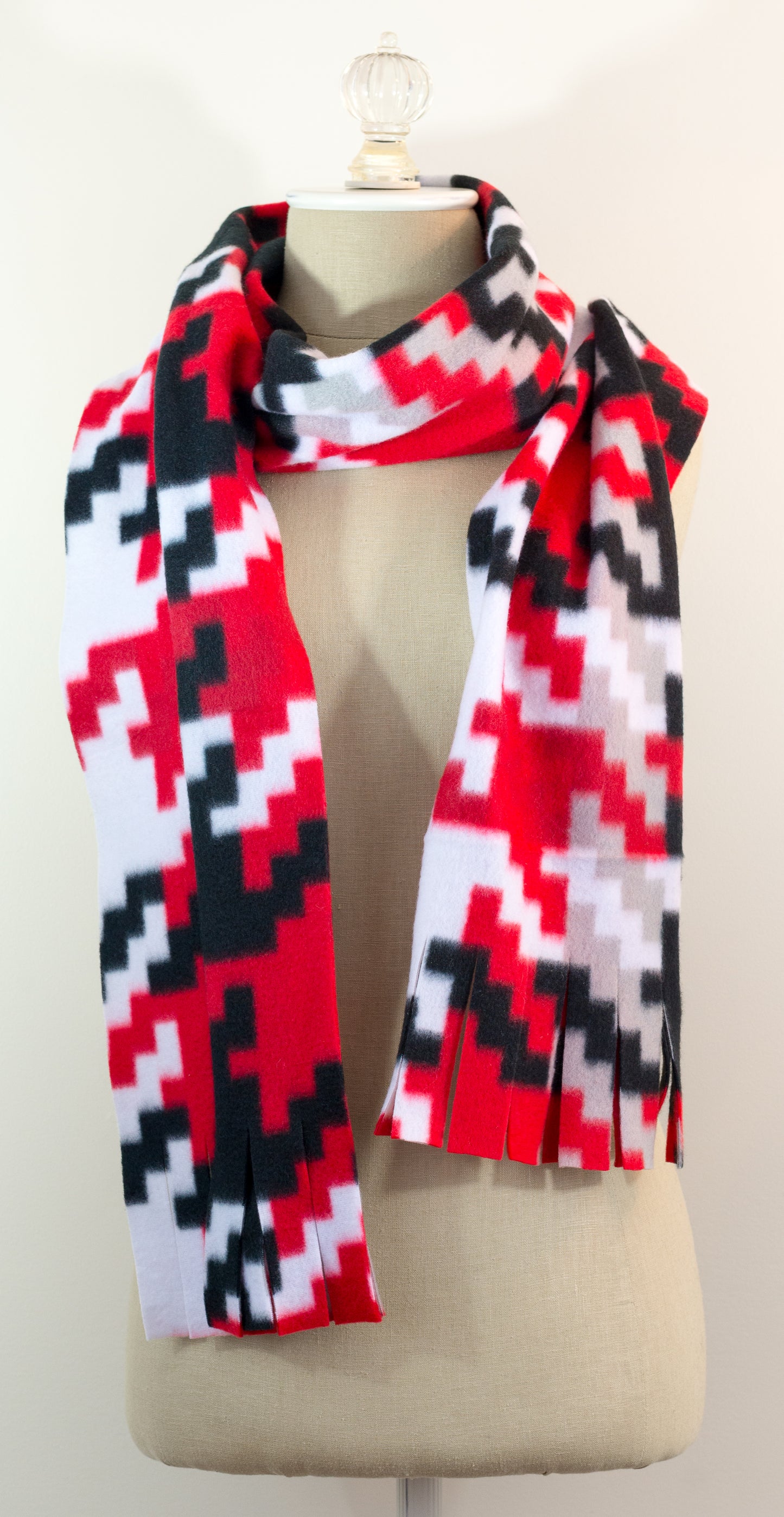 A scarf with a geometric houndstooth pattern in red, black, white, and beige colors, displayed on a flat surface.
Photo by Karen King [image_link]
